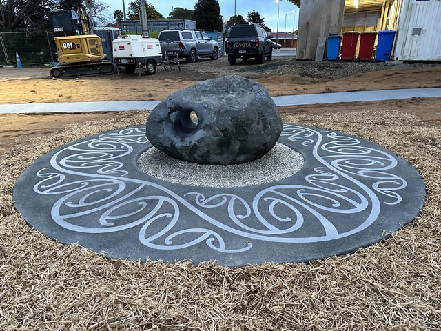 Carved stone piece on a koru-patterned concrete disc, public artwork