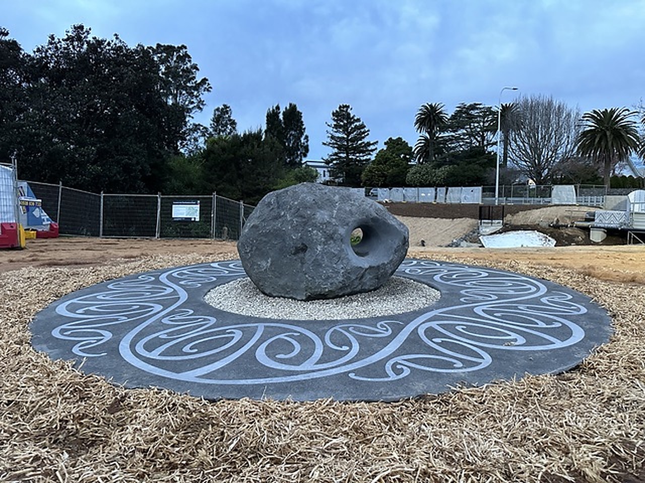 The stone ground-work seen from the side, koru disc and open reserve under a wide sky